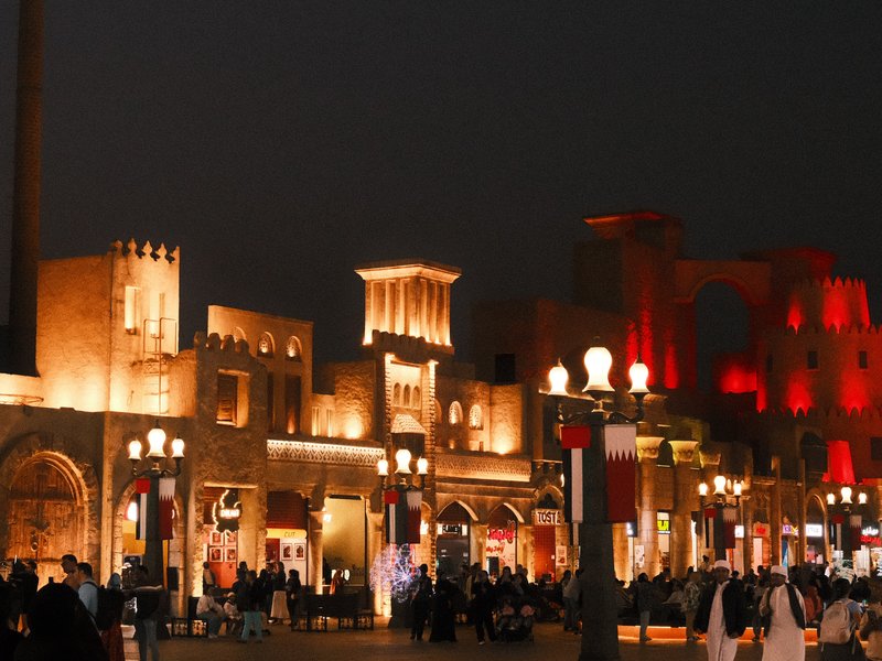 Nighttime view of illuminated buildings with people walking in a lively urban setting.
