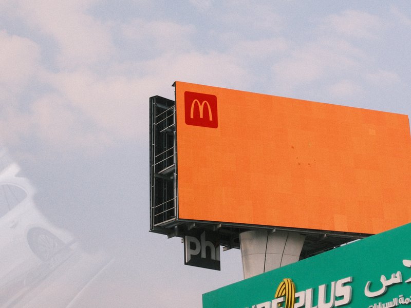 A McDonald's billboard against a pastel sky with clouds, showcasing the iconic logo.