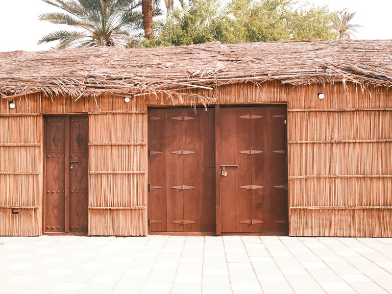 A rustic structure made of bamboo and thatch with two wooden doors, surrounded by greenery.