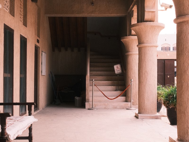 Interior view of a building with a staircase, columns, and a bench in a warm, muted color palette.