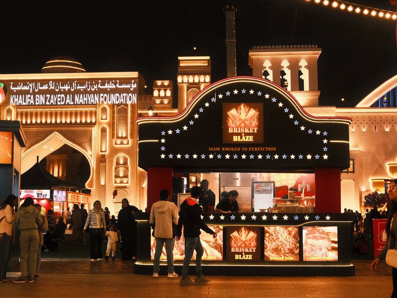 A vibrant food stall at night, illuminated by decorative lights with people gathered around.