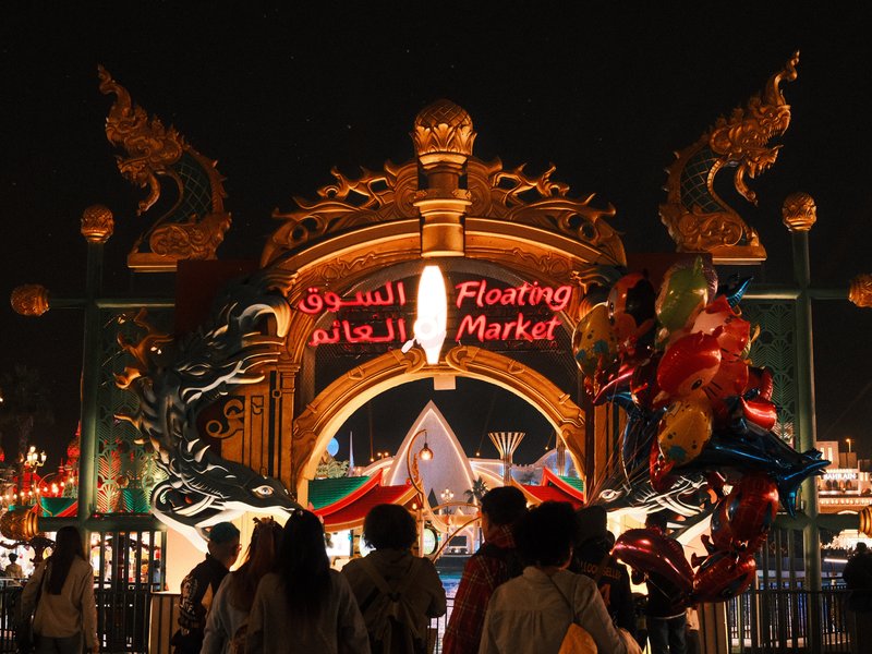 Night scene at a vibrant floating market entrance with colorful lights and decorations.