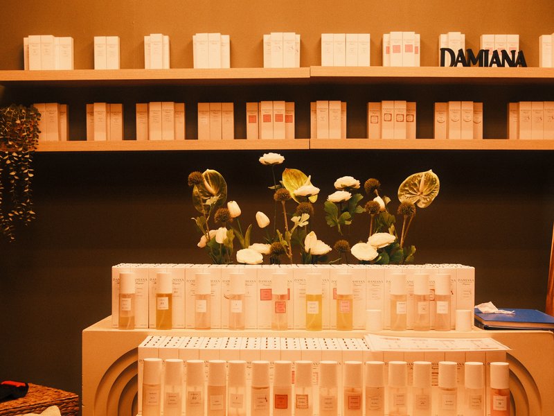 A display of beauty products with floral arrangements on a counter, set against a shelf of boxed items.