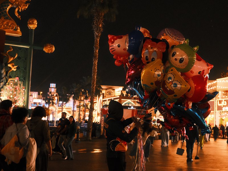 A person holding colorful balloons in a festive night market with bright lights and decorations.