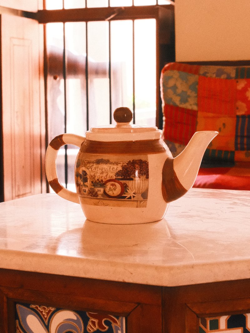 A decorative teapot on a marble table with a colorful quilted sofa in the background.