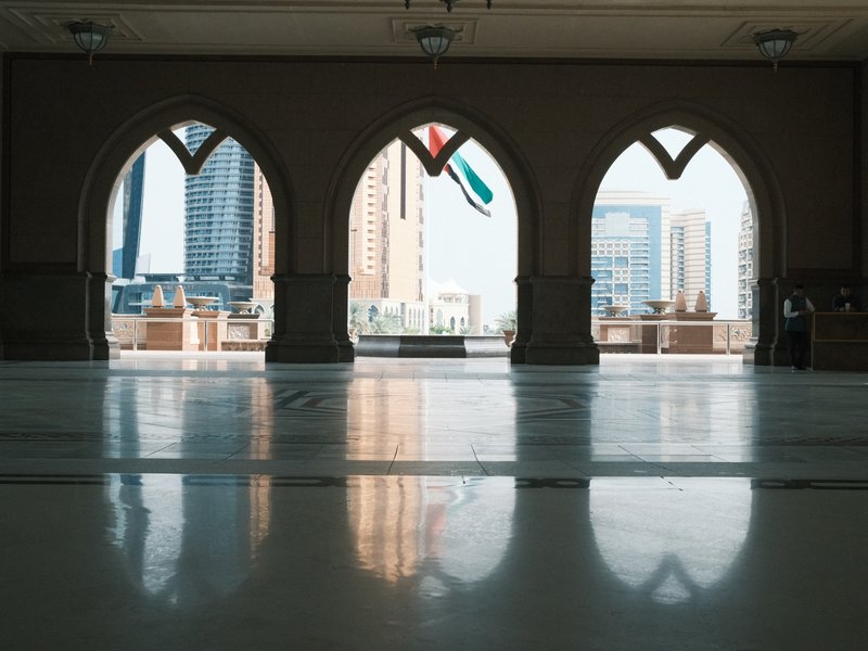 Three arched windows with reflections on a polished floor, showcasing a city skyline and a flag.