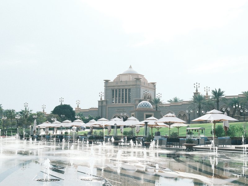 A grand building with a dome surrounded by umbrellas and a reflective pool of water.