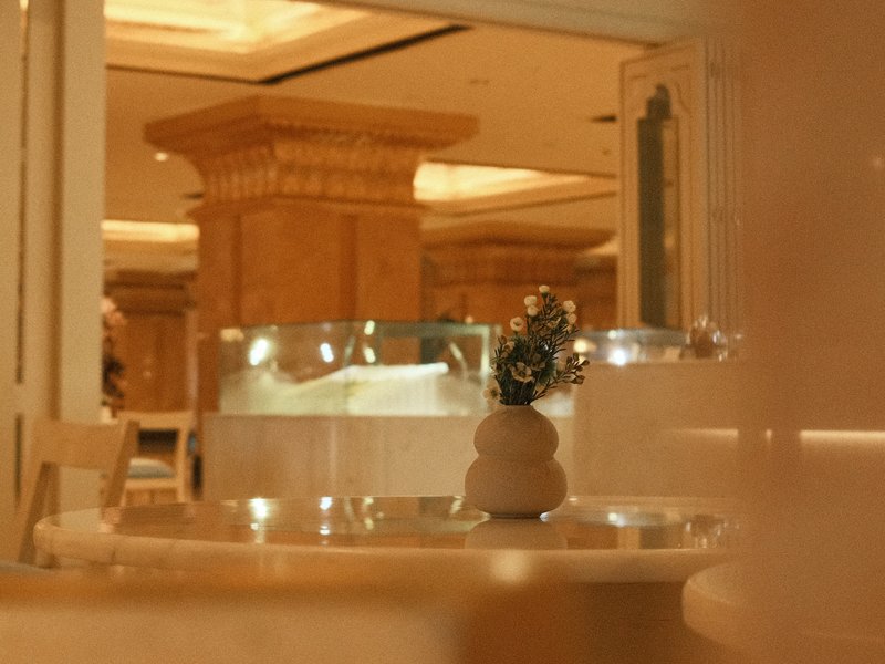 A softly lit indoor scene featuring a decorative vase on a table with elegant architecture in the background.