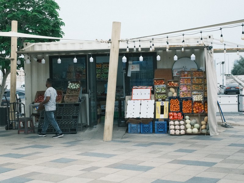 A fruit stall with colorful produce and a person walking by in an urban setting.
