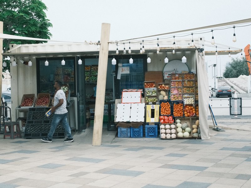 A fruit and vegetable stall with colorful produce outside a market, a person walking by.