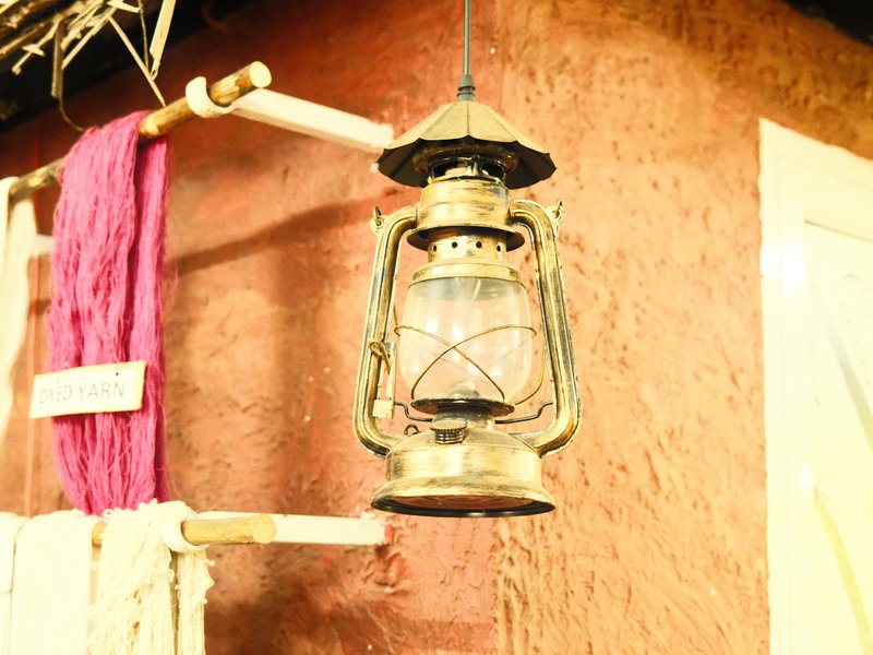 A vintage lantern hanging on a rustic wall with a pink cloth draped nearby.