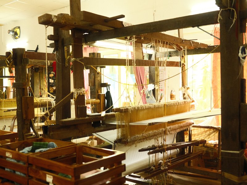 A traditional weaving loom in a bright room with wooden structures and natural light streaming in.
