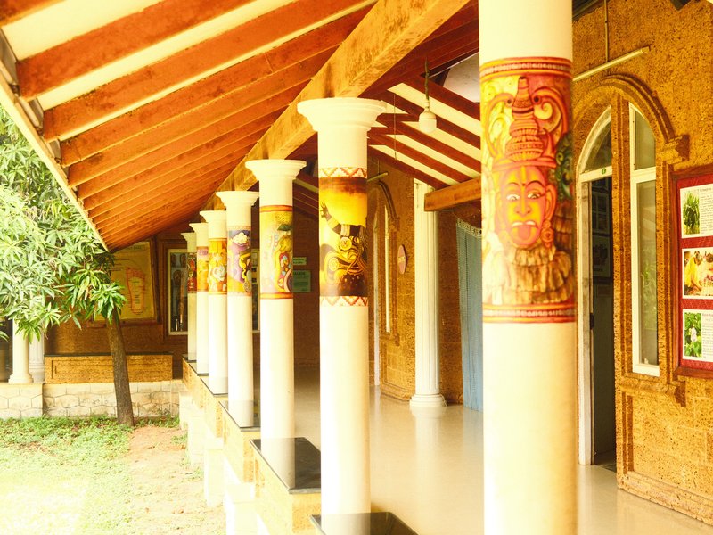 A corridor with decorative columns and artwork on the walls, surrounded by greenery.