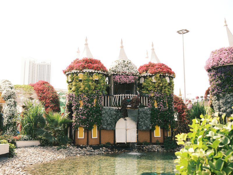 A whimsical castle adorned with vibrant flowers, surrounded by greenery and a small pond.