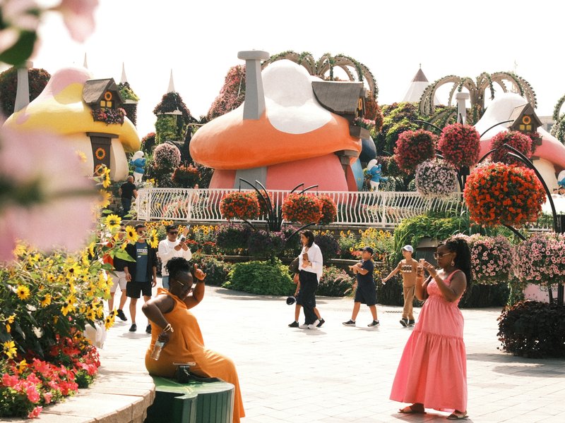 Colorful flower garden with whimsical structures and people enjoying the scenery.
