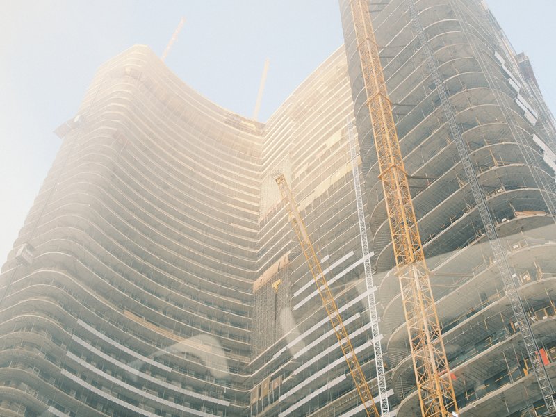 Construction site of a tall building with cranes and scaffolding under a hazy sky.