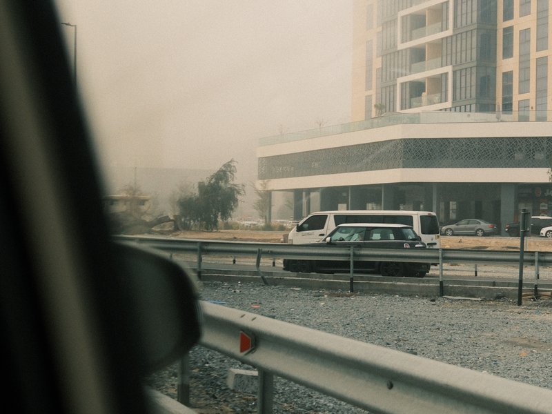A view from a car window showing a hazy urban scene with a building and vehicles.