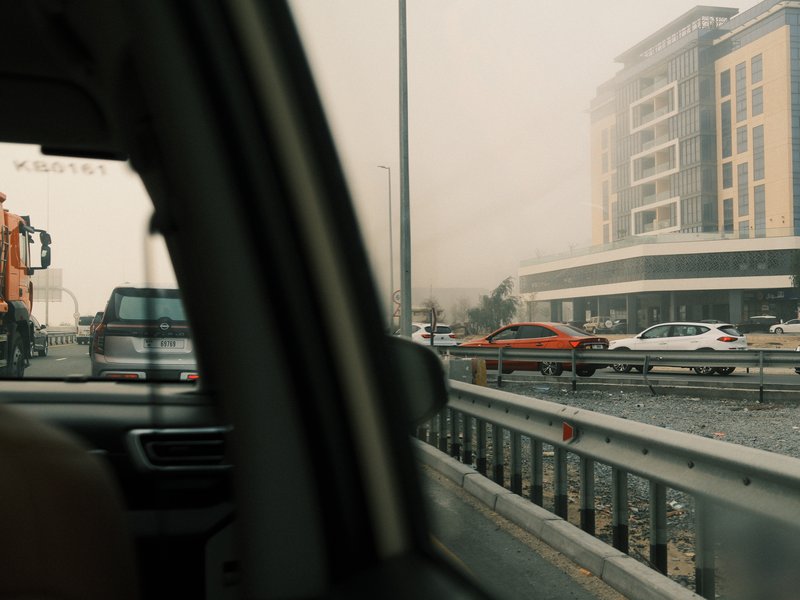 View from a car window showing a busy road with vehicles and a modern building in the background.