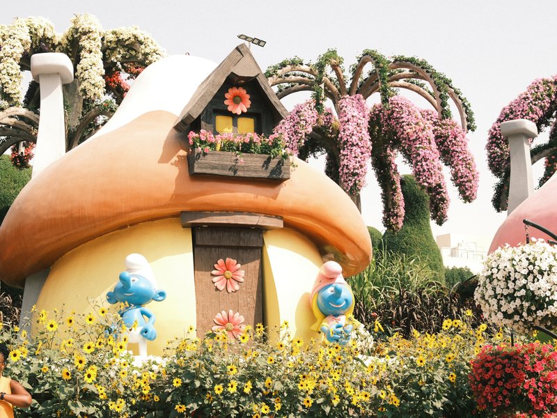 Colorful mushroom-shaped house surrounded by flowers and cartoon characters in a vibrant garden.
