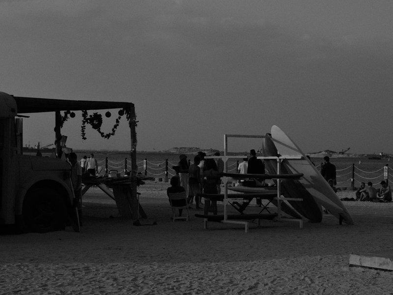Silhouetted figures at a beach with a food truck and lifeguard stand during dusk.