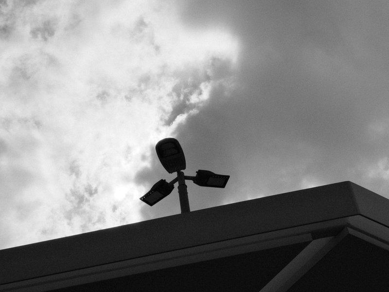 A silhouette of a streetlight against a cloudy sky, capturing a stark contrast in black and white.