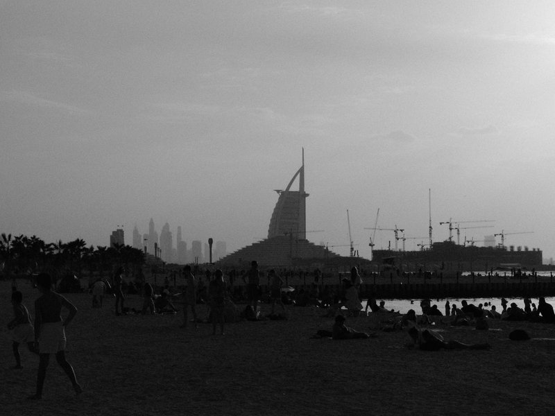 Silhouette of a tower against a sunset sky with people on a beach in the foreground.