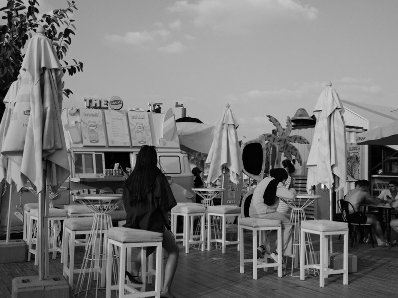 A lively outdoor café scene with white umbrellas and patrons enjoying their time.
