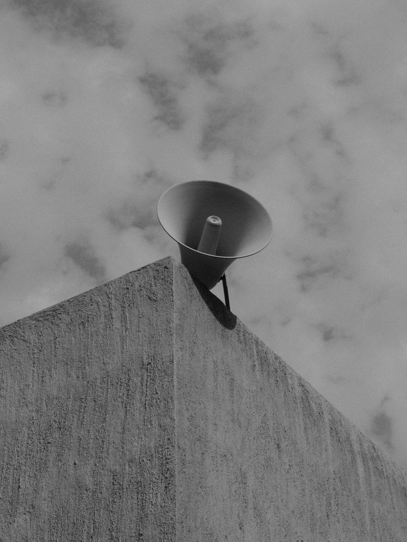 A megaphone mounted on a concrete structure against a cloudy sky.