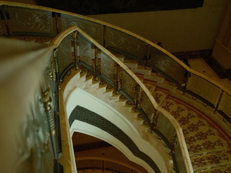 A spiral staircase with ornate railings and patterned flooring, viewed from above.