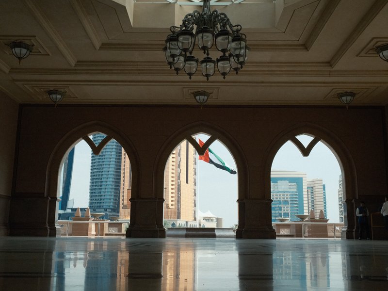 Interior view through arches showing city skyline with modern buildings and a flag in the background.