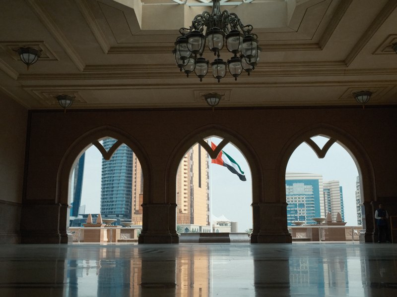 Interior view through arched windows showing city skyline with buildings and a flag.