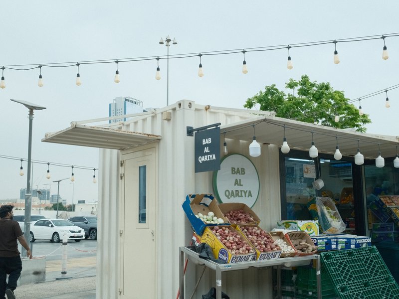 A small market stand with colorful fruits and vegetables under string lights on a cloudy day.