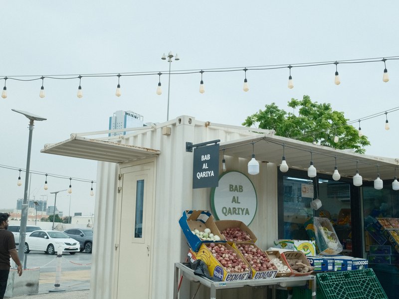 A market stall with fresh produce under string lights, set against a cloudy sky.