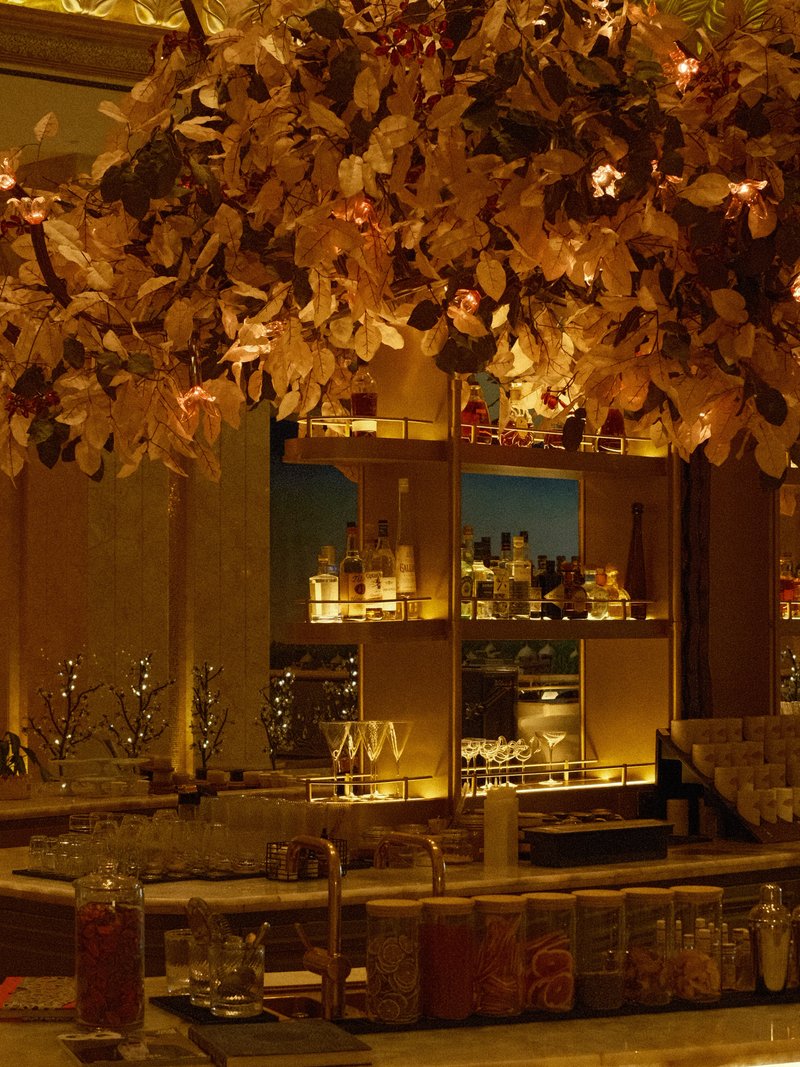 Elegant bar interior with a floral arrangement overhead and illuminated shelves of drinks.