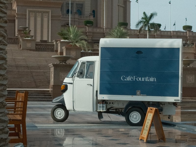 A small delivery truck parked on a wet plaza with palm trees in the background.