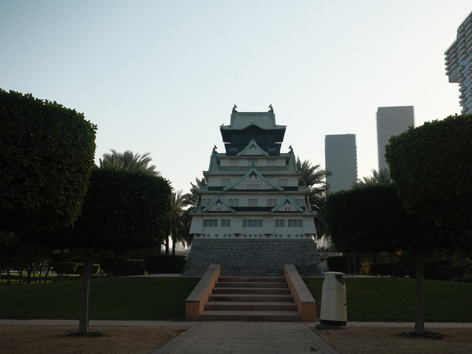 A traditional-style building with a tiered roof surrounded by palm trees and modern skyscrapers.