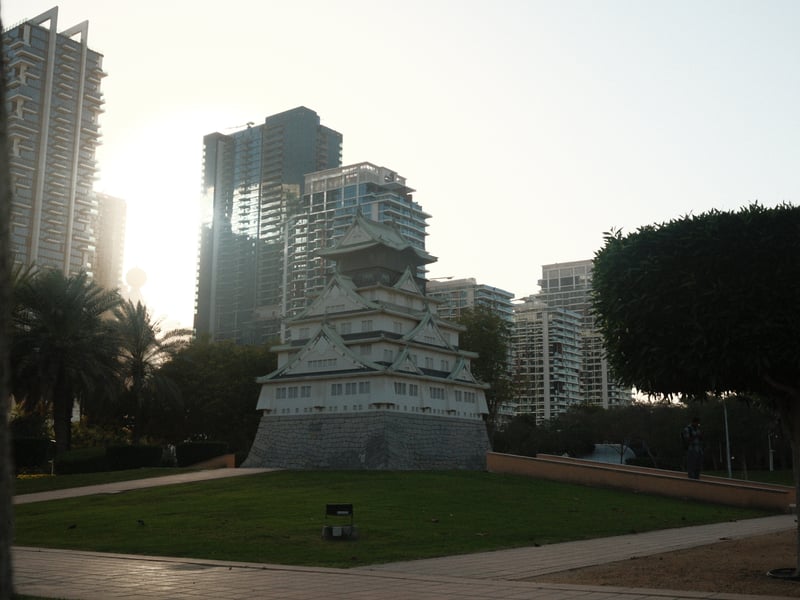 A monument surrounded by modern buildings and palm trees during golden hour.