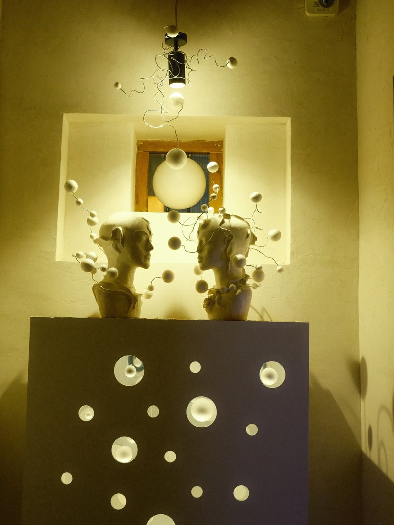 Two sculpted heads facing each other on a pedestal, illuminated by soft light with decorative elements.