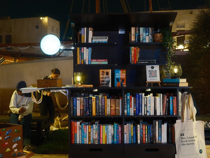 A bookshelf filled with books at night, with a person in the background organizing items.