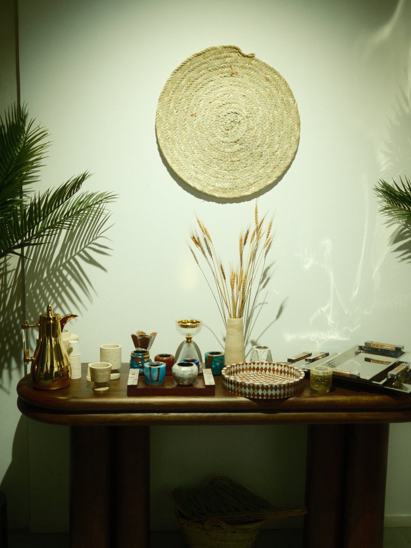 A wooden table displaying various decorative items, plants, and a woven wall hanging.