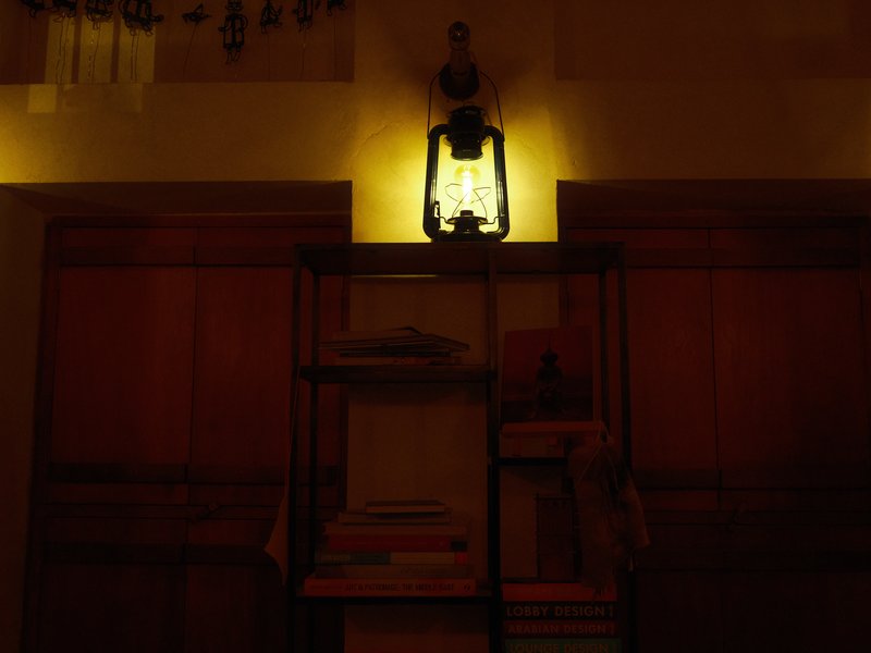 A dimly lit room featuring a vintage lantern casting a warm glow on a bookshelf.