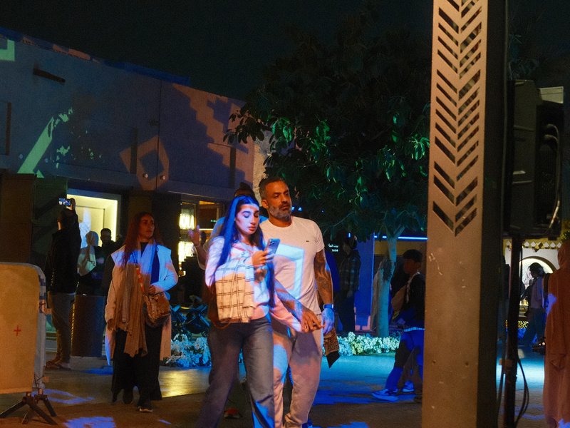 A couple walking together in a vibrant outdoor setting with colorful lights at night.