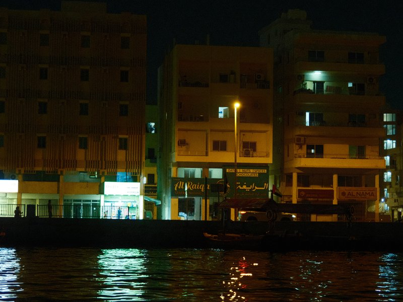 Nighttime view of buildings along a waterfront with reflections in the water.