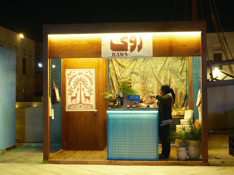 A small outdoor kiosk at night with a person preparing food, illuminated by warm lights.