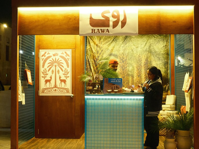A vibrant food stall with a wooden counter and decorative backdrop, featuring a customer and vendor interaction.