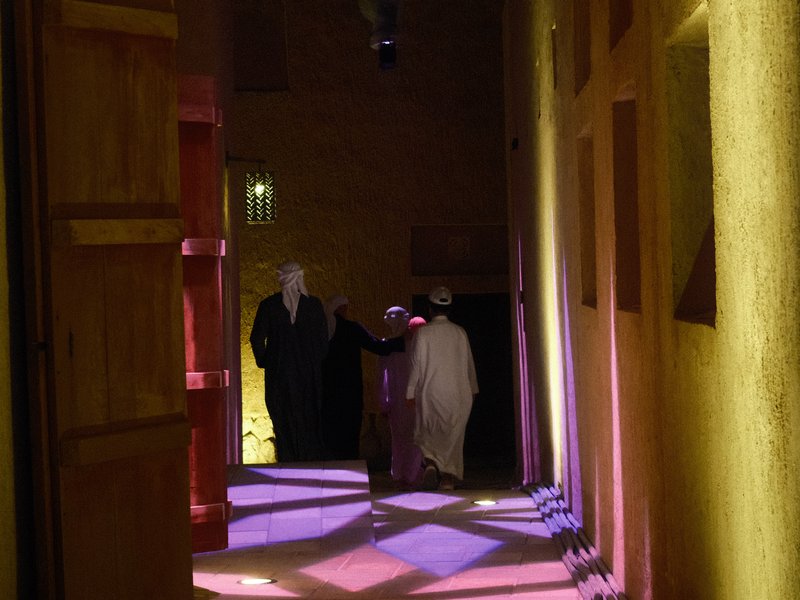 Three figures walking through a dimly lit corridor with colorful light patterns on the floor.