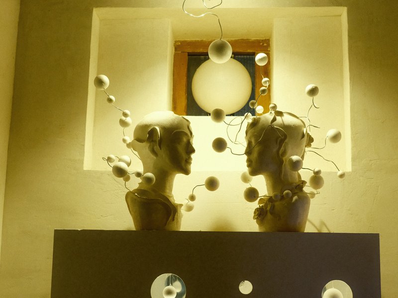 Two artistic busts facing each other with decorative elements in a softly lit indoor setting.