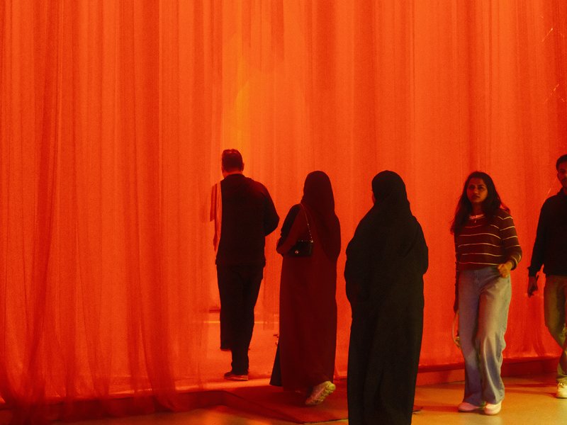 Silhouettes of people walking through an orange curtain, creating a warm and inviting atmosphere.