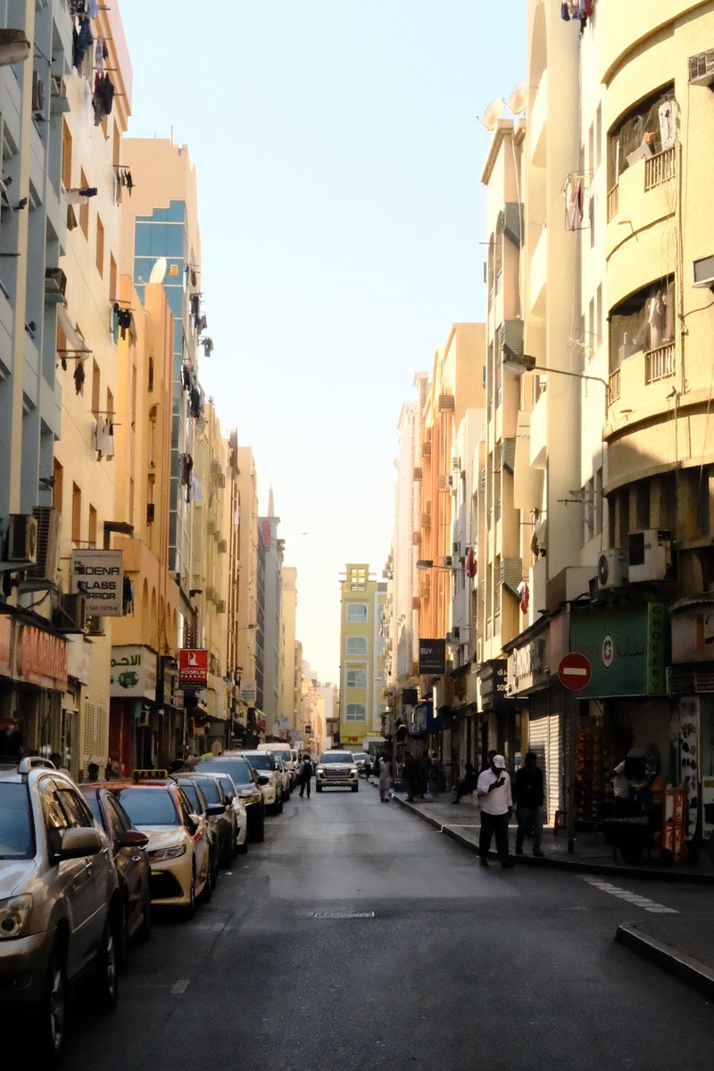 A narrow urban street lined with colorful buildings and parked cars under a clear blue sky.