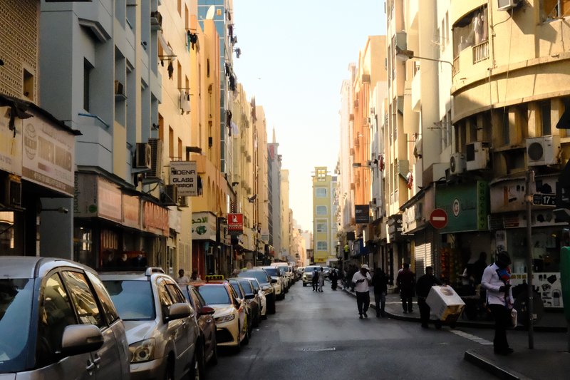 A bustling urban street lined with colorful buildings and parked cars under a clear sky.
